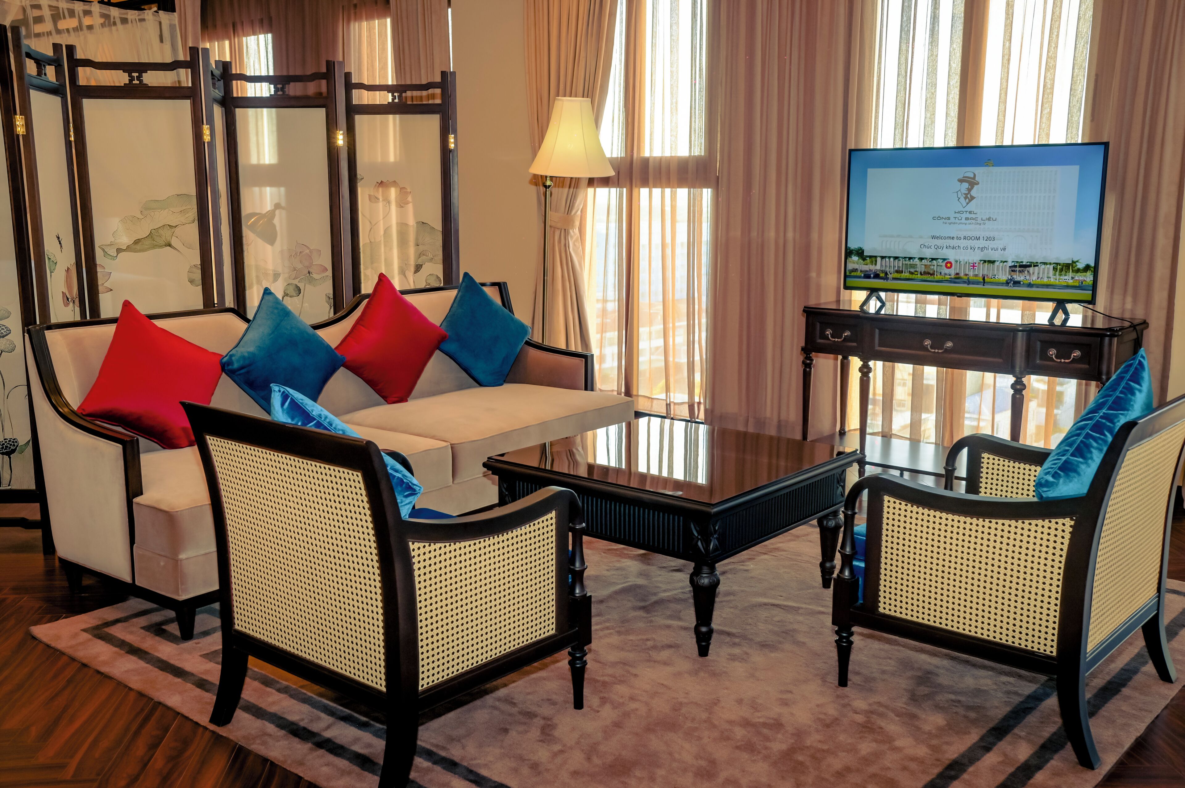 A hotel room with a sofa, two armchairs, a coffee table, a TV, and a decorative screen.
