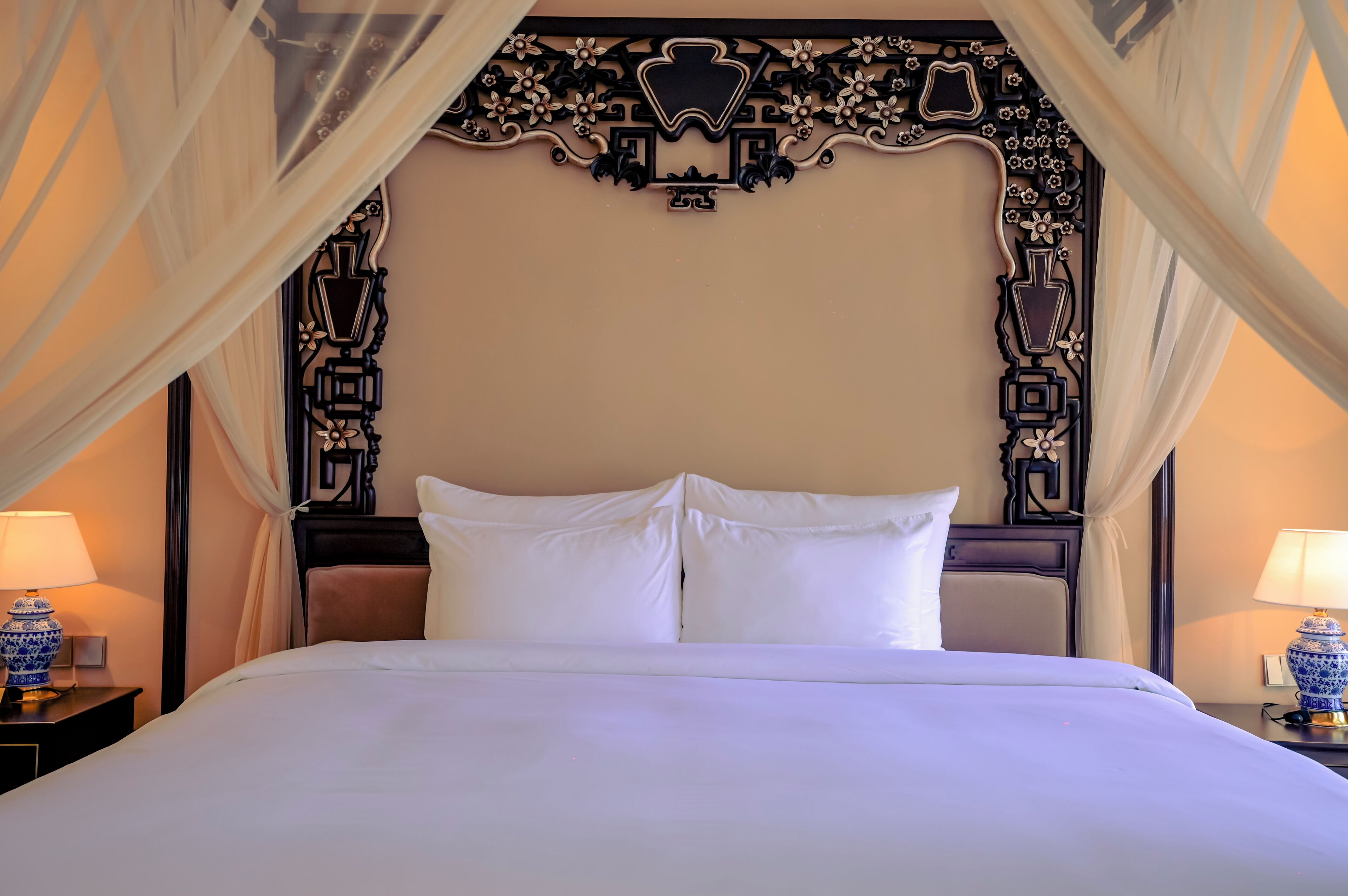 A bed with white linens, a decorative headboard, and two bedside lamps.