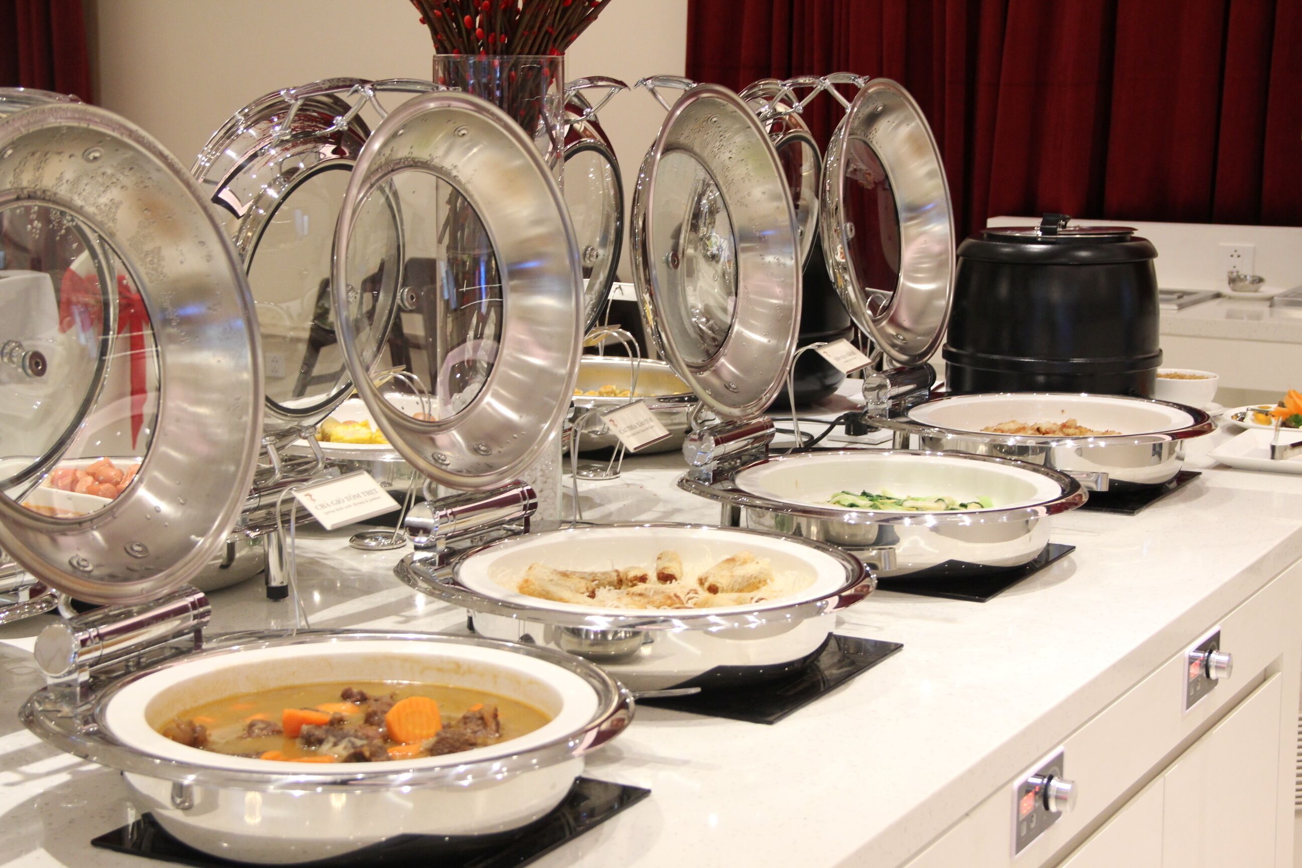 Una barra de buffet con diversos platos en recipientes metálicos.