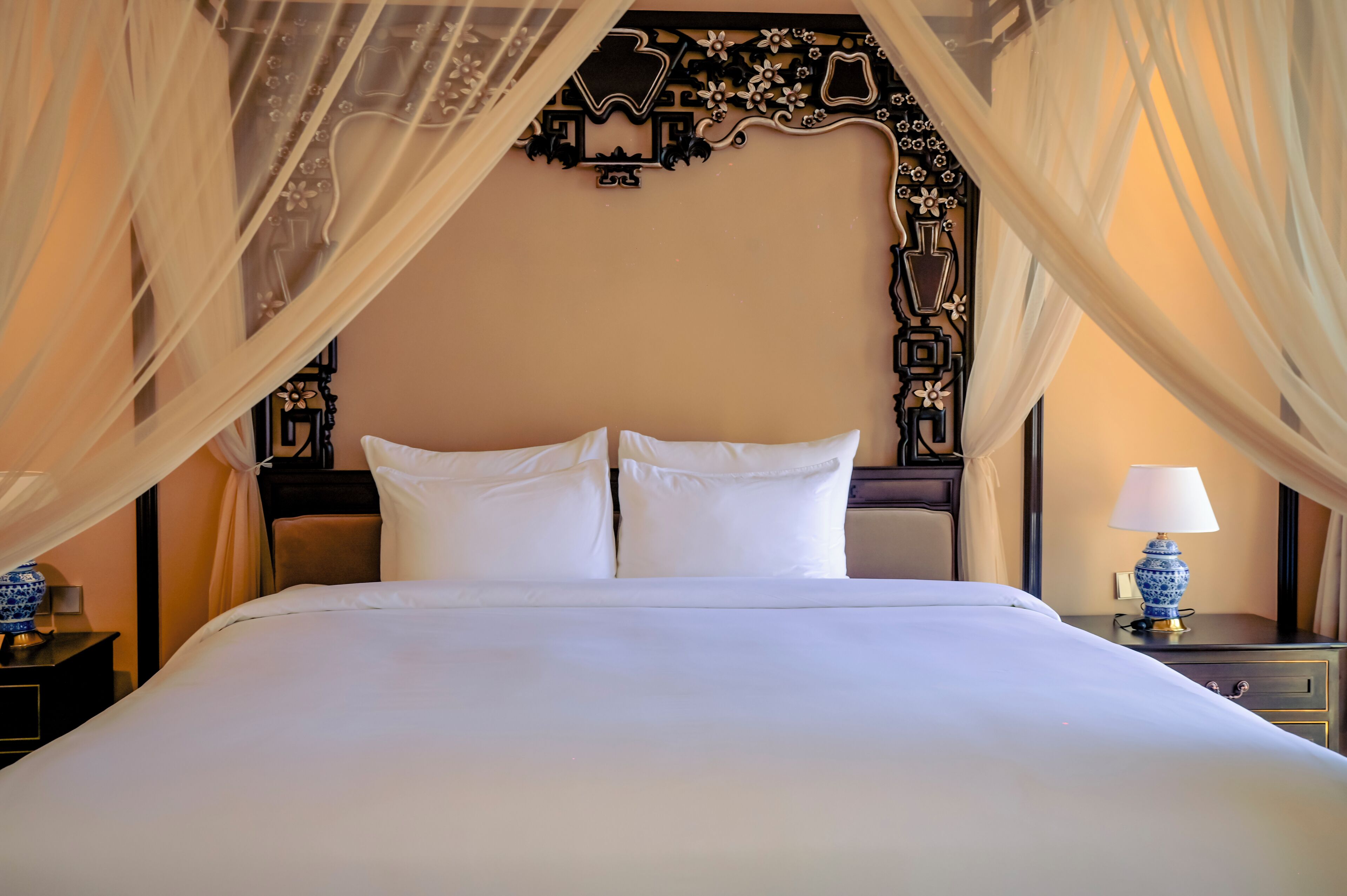 A bed with white linens, a decorative headboard, and a nightstand with a lamp.