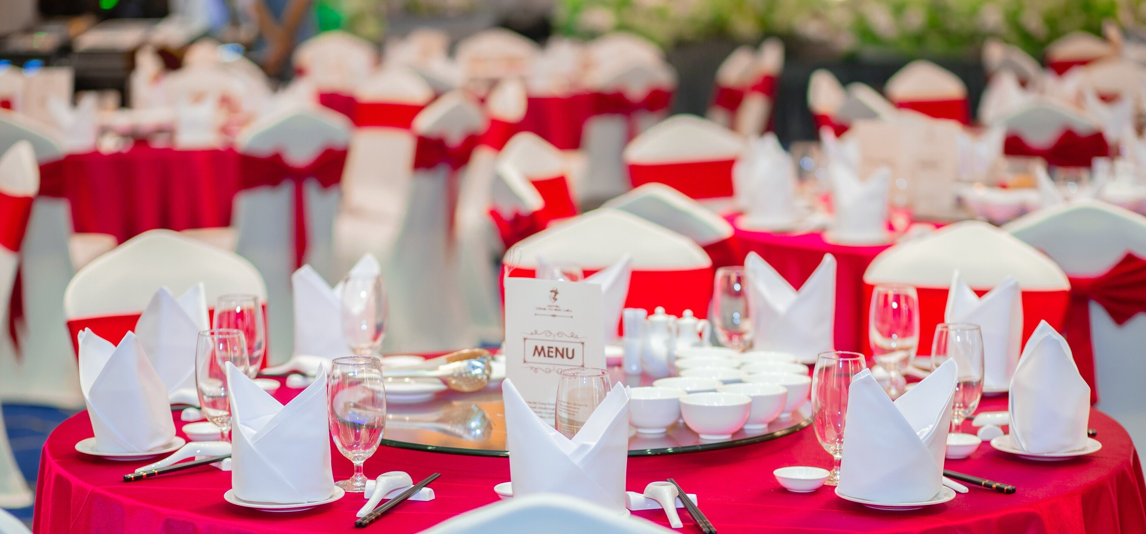 A banquet table set with white napkins, plates, and wine glasses, with a menu sign in the center.