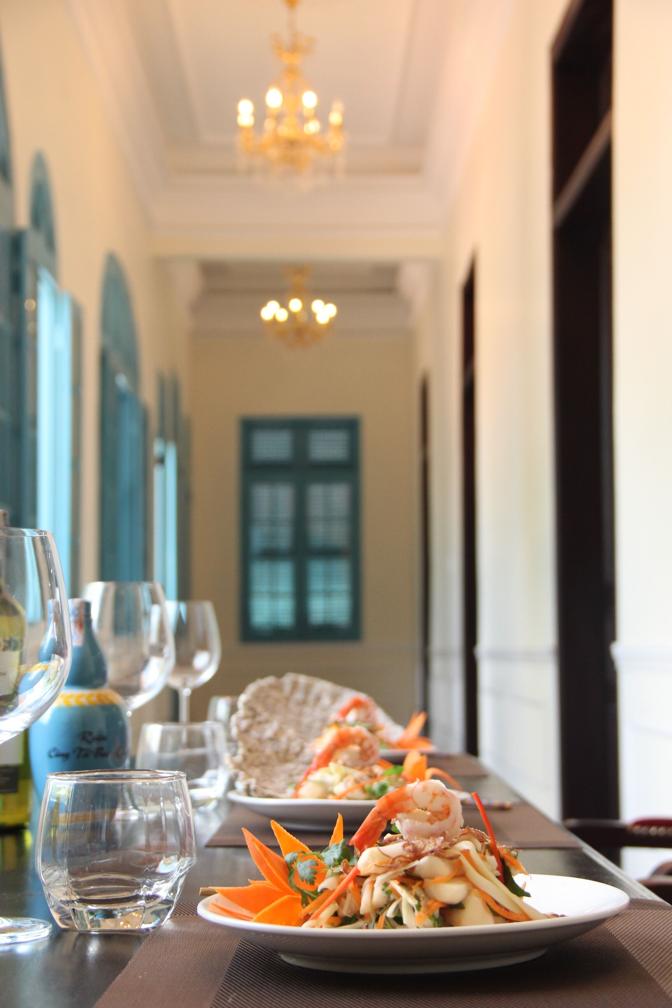 A dining table with plates of food, glasses, and a bottle.