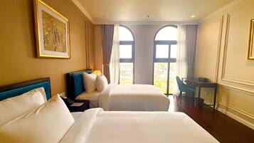 A hotel room with two beds, a desk, and large windows.