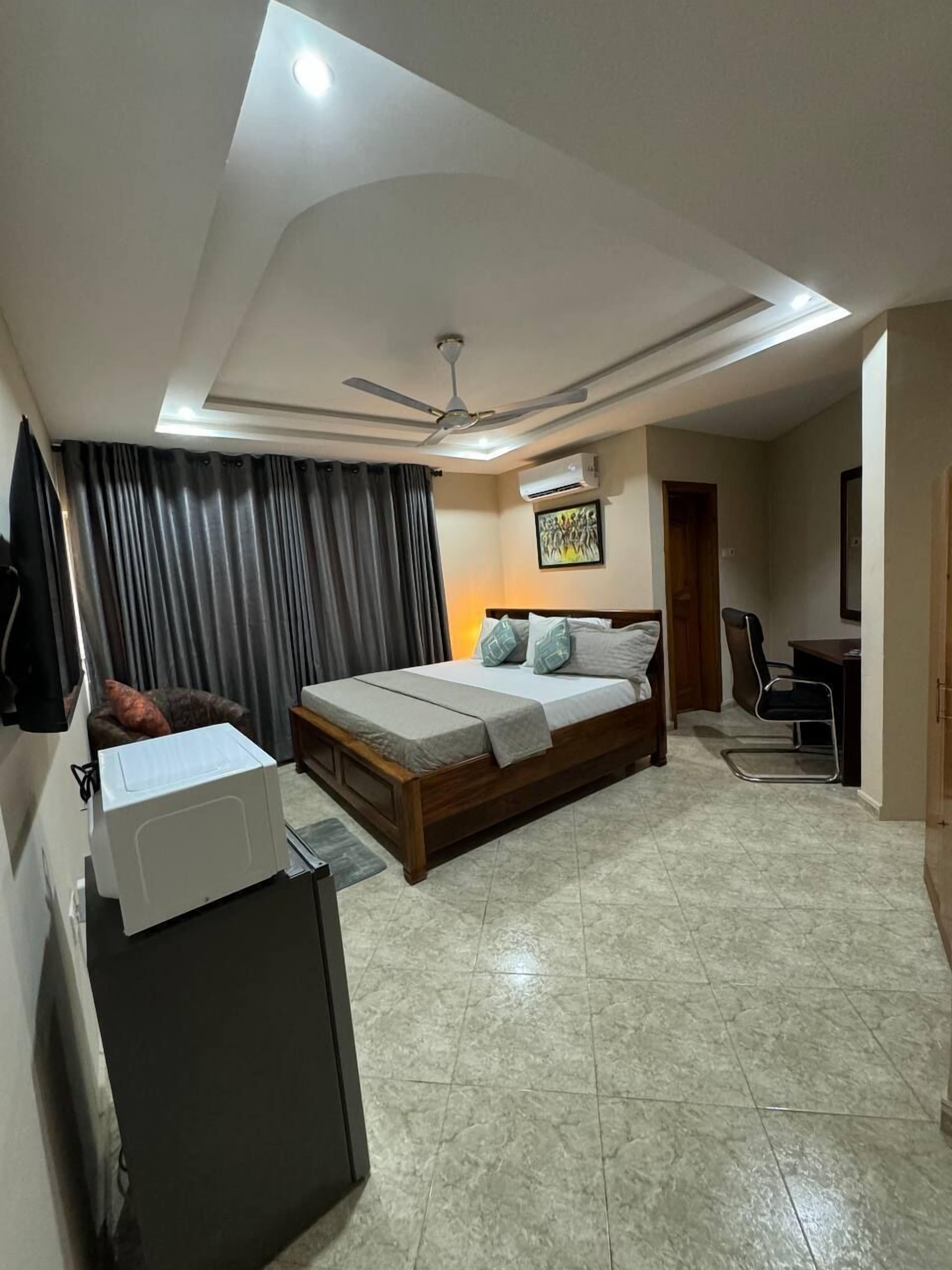 A bedroom with a bed, a desk, a chair, a ceiling fan, and an air conditioning unit.