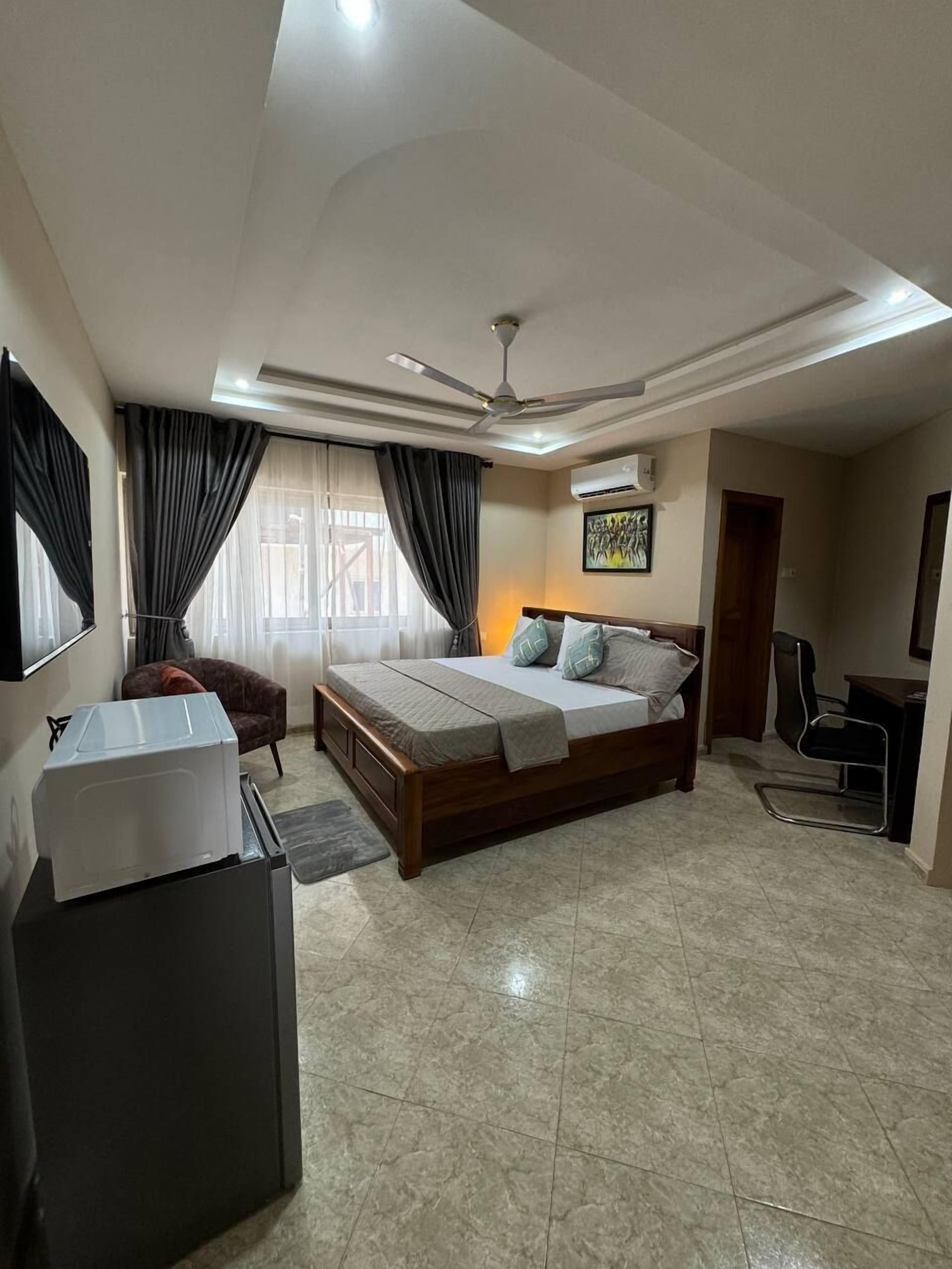 A bedroom with a bed, a desk, a chair, a ceiling fan, and an air conditioning unit.