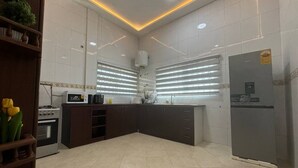A modern kitchen with white tiles, a built-in oven, a microwave, a refrigerator, and a sink. - Chester Hill Residence  (Kwabenya)