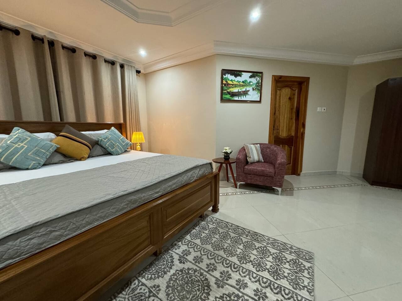 A bedroom with a bed, a nightstand, a lamp, a red sofa, a painting, and a wooden door.