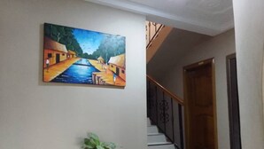 A hallway with a staircase, a painting on the wall, and a potted plant. - Chester Hill Residence  (Kwabenya)