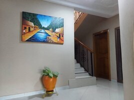Um corredor com escadas, um quadro na parede e um vaso de planta.