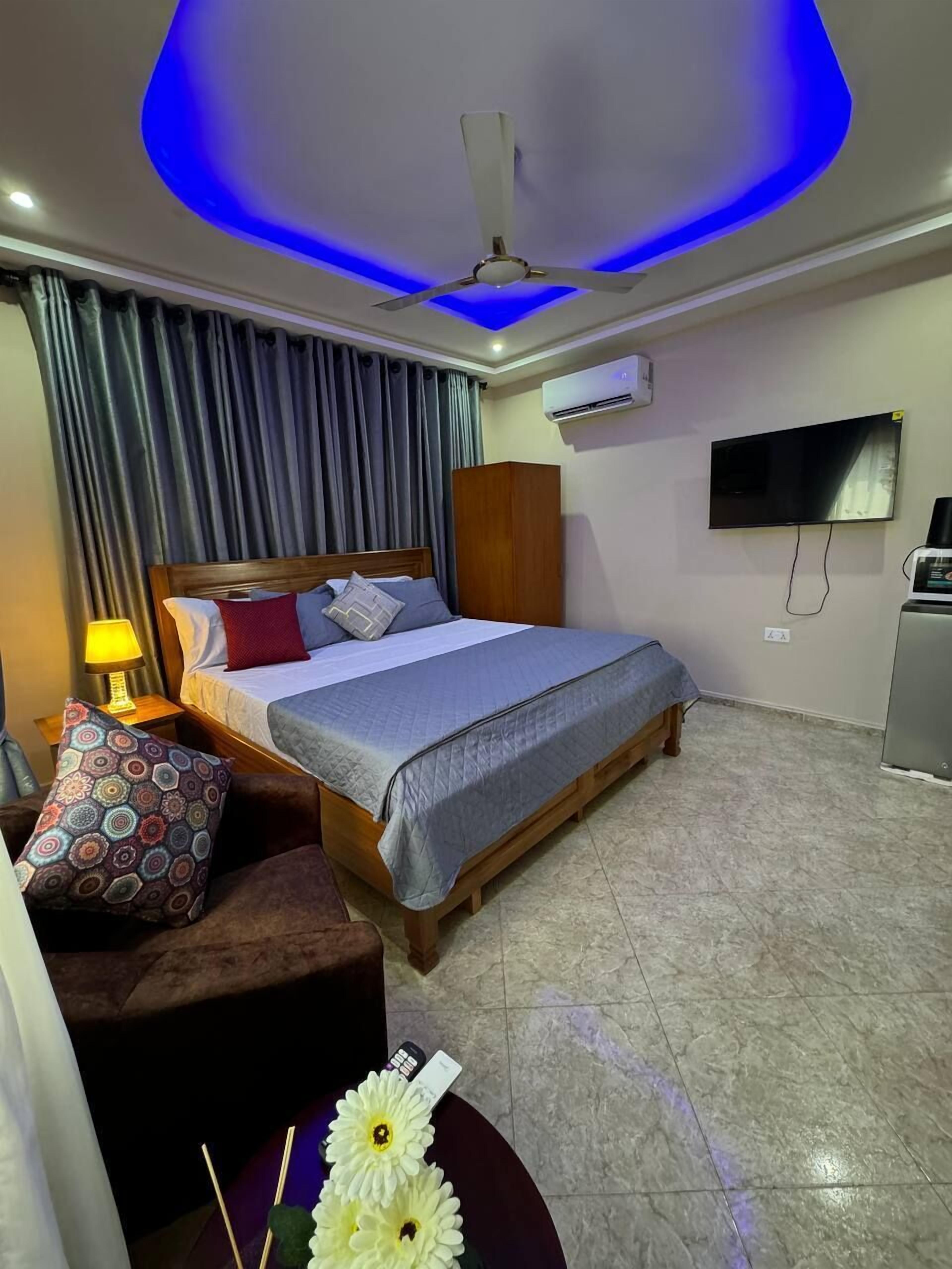 A hotel room with a bed, a TV, an air conditioner, and a ceiling fan.