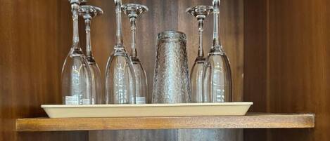 Un mueble de madera con un estante que contiene varias copas de vino y una bandeja abajo con diferentes tazas.