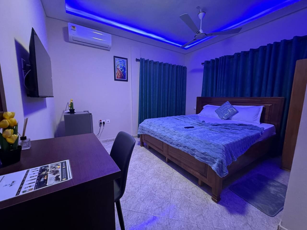 Een hotelkamer met een bureau, bed, airconditioning en een plafondventilator.
