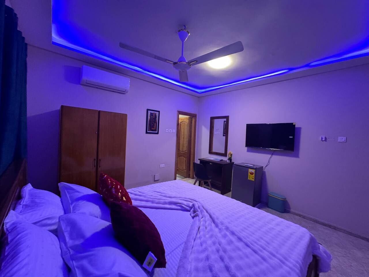 Une chambre avec deux lits, un ventilateur de plafond, une télévision, une armoire et un appareil de climatisation.