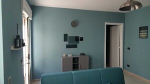 A living room with a teal sofa, a ceiling light, and a door leading to another room.