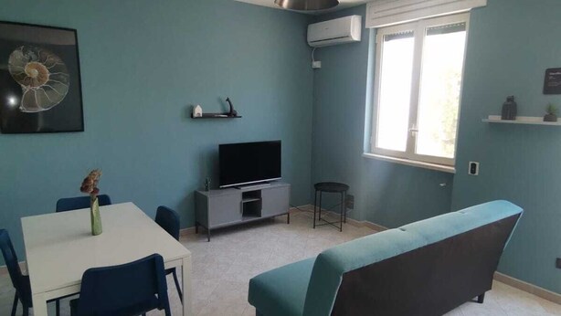 A living room with a white table, blue chairs, a sofa, a TV, and a ceiling fan.