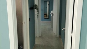 A hallway with teal walls and white trim, leading to a room with a tiled floor and a mirror on the wall.