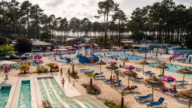 Ein Wasserpark mit mehreren Pools, einer Wasserrutsche und Liegebereichen mit Sonnenschirmen.