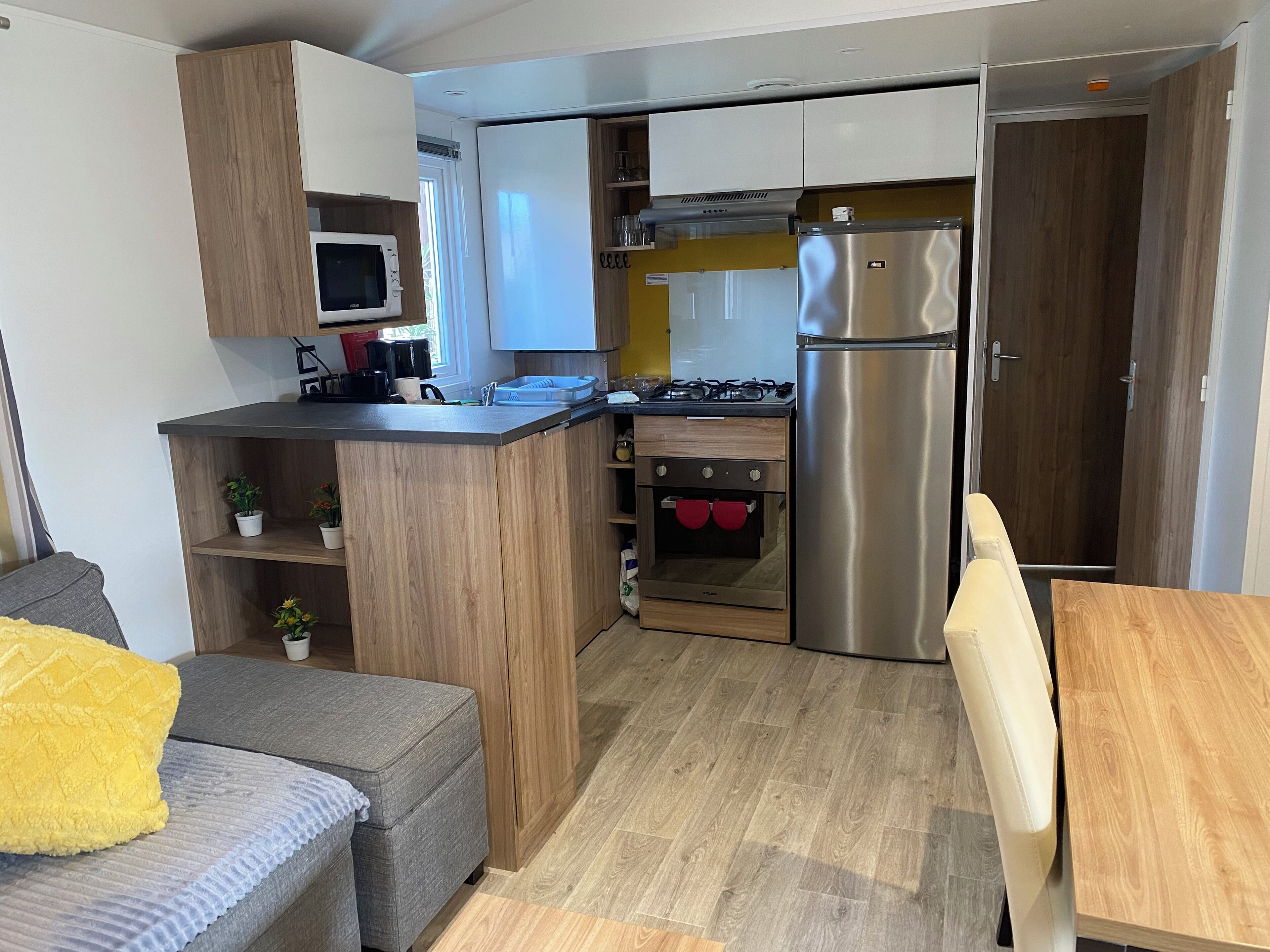 Eine kompakte Küche mit Mikrowelle, Herd, Backofen und Kühlschrank. Es gibt eine kleine Sitzecke mit einer Couch und einem Tisch.
