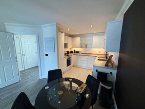 A compact kitchen with white cabinets, a microwave, and a toaster. There is a round table with chairs in the foreground.