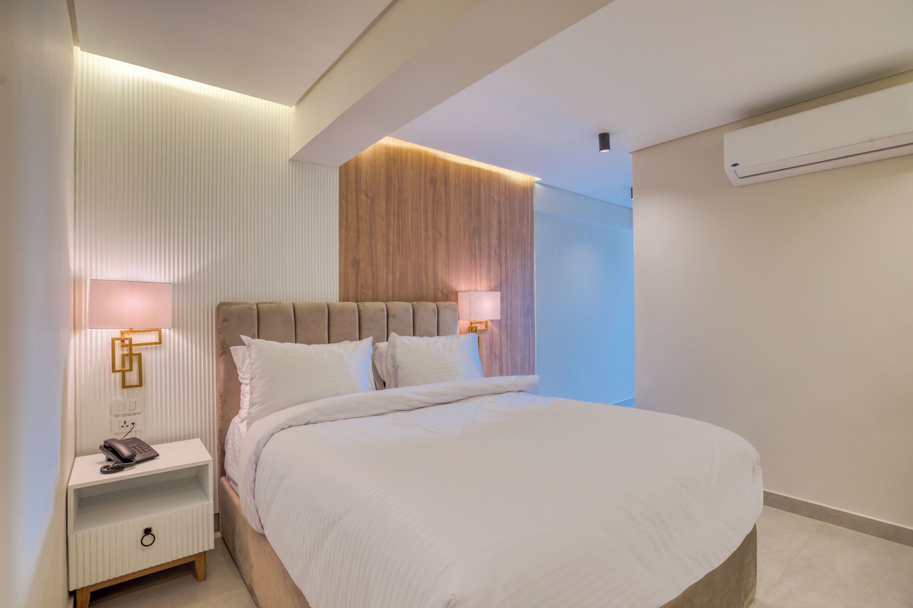 Een moderne hotelkamer met een groot bed, een nachtkastje met een lamp en een vastgezet houten hoofdbord.