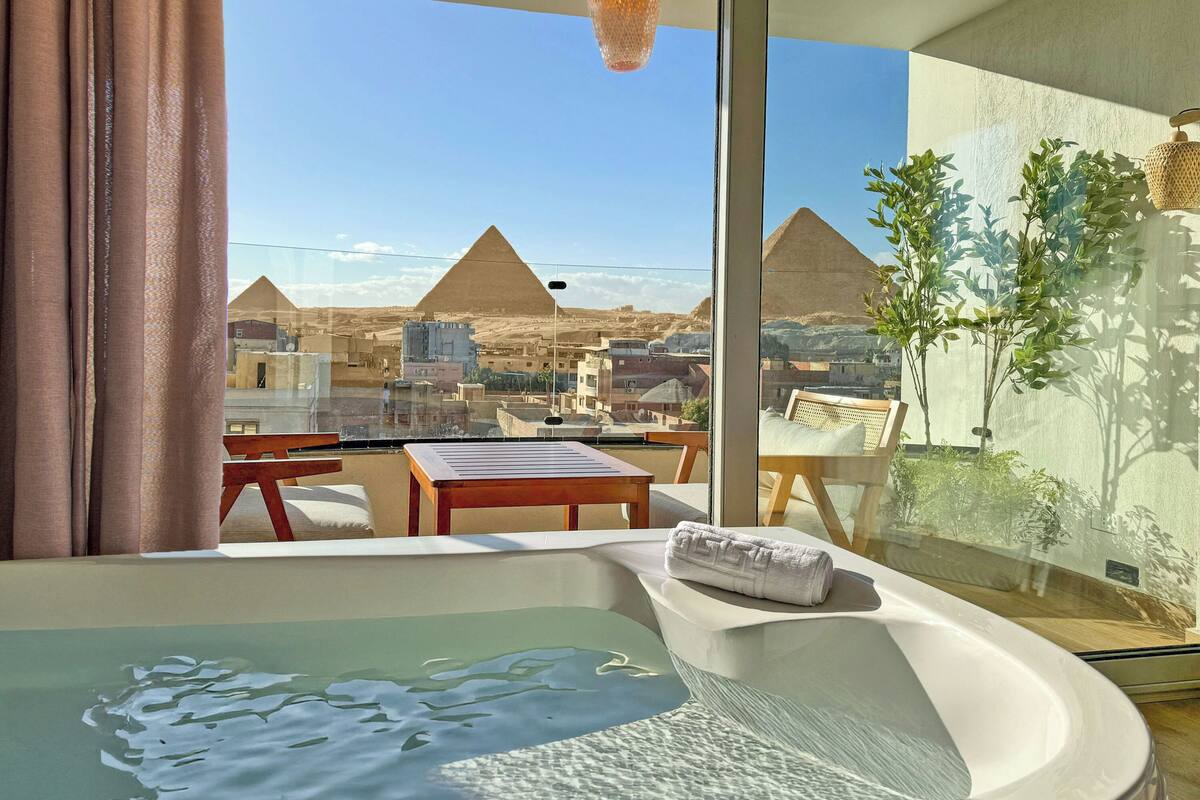 Une chambre avec un jacuzzi, une vue sur les pyramides et un balcon agrémenté de plantes.