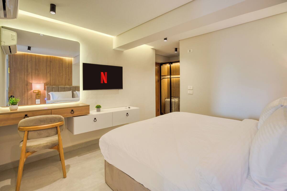 Une chambre d’hôtel moderne avec un grand lit, un bureau avec une chaise, un téléviseur fixé au mur et une armoire en bois.