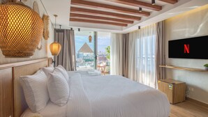 Une chambre d’hôtel moderne, dotée d’un grand lit, d’un téléviseur fixé au mur et offrant une vue sur le paysage urbain par la fenêtre.
