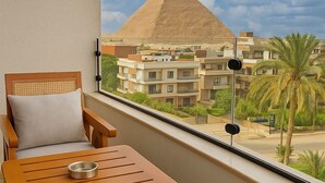 Un balcon avec une table et des chaises en bois, une vue sur une pyramide et un palmier.
