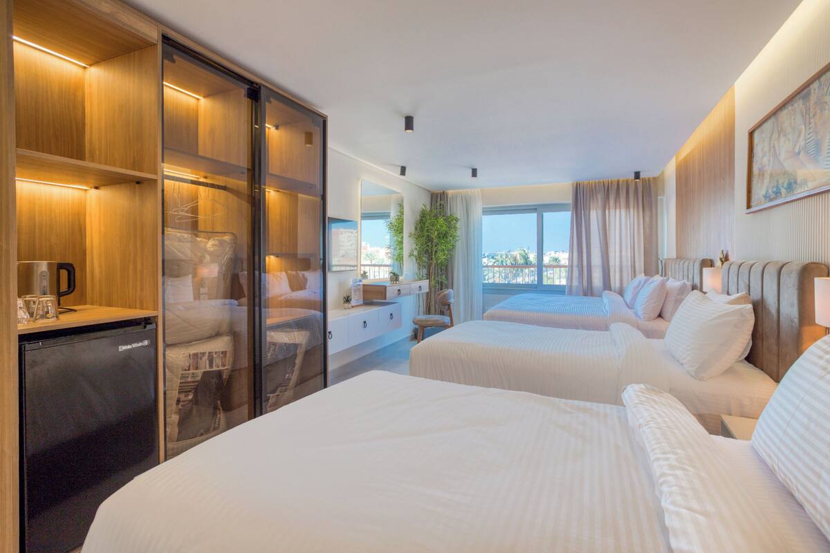 Une chambre d’hôtel avec deux lits, un bureau, une chaise, une petite table et un réfrigérateur.
