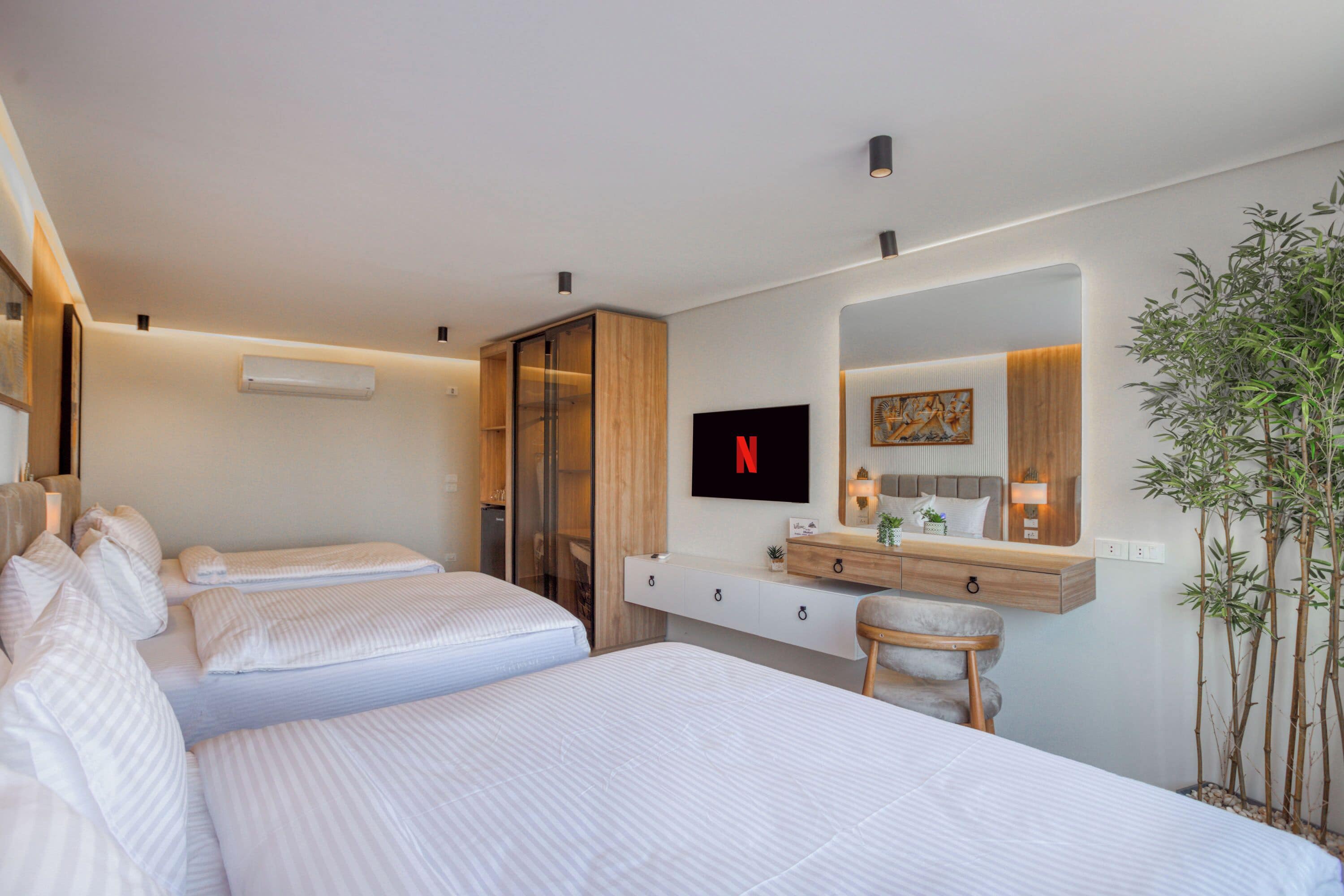 Ein Hotelzimmer mit zwei Betten, einem Fernseher, einer Holzkommode, einem Schreibtisch und einem Spiegel.