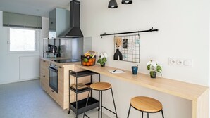 A modern kitchen with a central island, bar stools, pendant lighting, and a black range hood. - F4 Family apartment between Paris & Disneyland (Lognes)