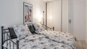 A bedroom with a bed, a framed picture of the Eiffel Tower, a bedside lamp, and a white door. - F4 Family apartment between Paris & Disneyland (Lognes)