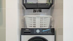 A compact, modern laundry room with a front-loading washing machine, a shelf above it, and a potted plant. - F4 Family apartment between Paris & Disneyland (Lognes)