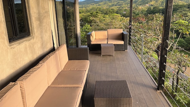 Un espace extérieur aménagé, abrité et doté d’un canapé et d’une petite table, offrant une vue sur un paysage luxuriant.