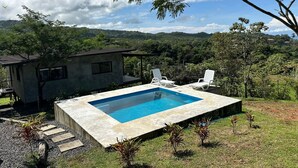 Une maison moderne dotée d’une piscine, entourée d’une végétation luxuriante et de collines.