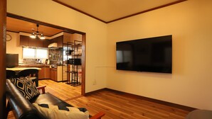 Una sala de estar con un sofá de cuero, un televisor de pantalla plana montado en la pared y piso de madera.
