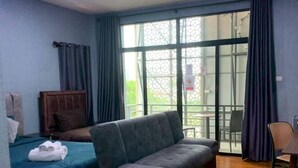 A room with a bed, a sofa, a chair, a table, and a large window with curtains. - Grabsleep&Khokeng (Bangkok)