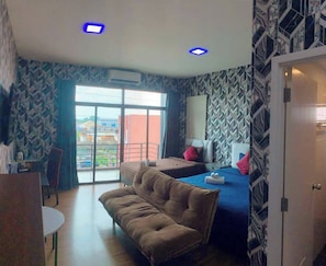 A hotel room with a bed, a sofa, a desk, and a view of the outside.