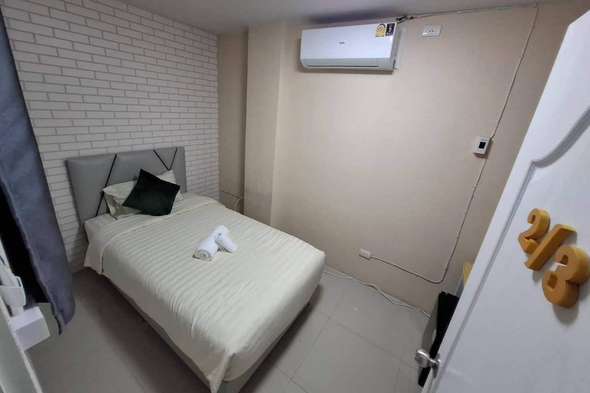 Ein Hotelzimmer mit Bett, weißer Ziegelwand, Klimaanlage und Tür mit einer Nummer.