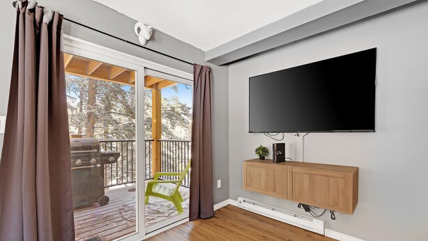 A room with a sliding glass door leading to a deck, a mounted TV, and a wooden cabinet. - Cozy two bedroom Breckenridge, steps away from Bus stop to mountain and downtown (Breckenridge)