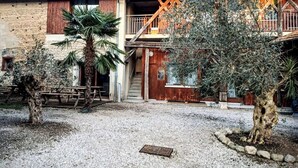 Un edificio con fachada rústica, balcones de madera y un patio de grava con árboles.