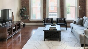 Un salón amplio con un gran ventanal, un ventilador de techo y un televisor.