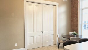 Una habitación con una puerta blanca cerrada, una mesa redonda con sillas y una ventana que da a un edificio.