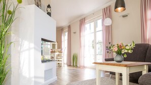 A modern living room with a white entertainment unit, a dining area with a table and chairs, and a sofa. - Ferienhaus Schilfrohrsanger, Fuhlendorf (Fuhlendorf)