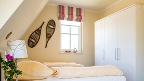 A bedroom with a bed, a nightstand, a lamp, decorative wall art, a window with a view, and a wardrobe. - Ferienhaus Schilfrohrsanger, Fuhlendorf (Fuhlendorf)