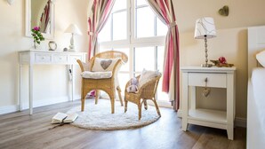 A bedroom with a large window, two wicker chairs, a bedside table, and a nightstand. - Ferienhaus Schilfrohrsanger, Fuhlendorf (Fuhlendorf)