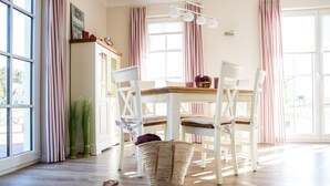 A dining area with a wooden table, white chairs, and striped curtains. - Ferienhaus Schilfrohrsanger, Fuhlendorf (Fuhlendorf)