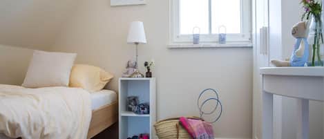 A bedroom with a bed, a bedside table with a lamp, a window, a shelf with items, and a basket.