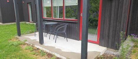 A patio with two chairs and a table, a wooden deck, and a window with red trim.