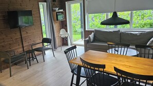 A modern kitchen with wooden walls, a flat-screen TV, a dining table with chairs, and a sofa. - Skidvägen 4a - Lodge (Jarvso)